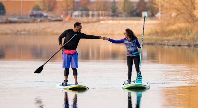 man and woman fist bump while on paddle boards at Lake Lorraine