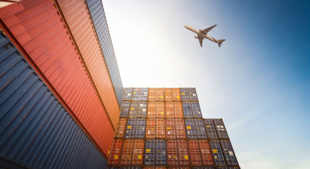 Airplane flies over stacks of shipping containers