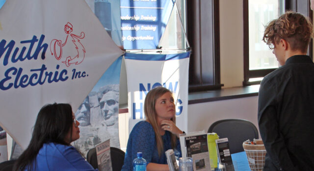 A picture of two employees at a Muth Electric table talking to two attendees at a career fair