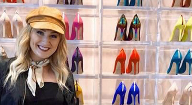 A photo of Kayla Kruse in front of a wall of high heeled shoes of different colors
