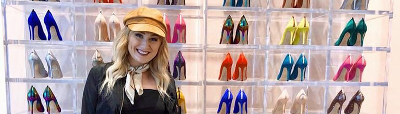 A photo of Kayla Kruse in front of a wall of high heeled shoes of different colors