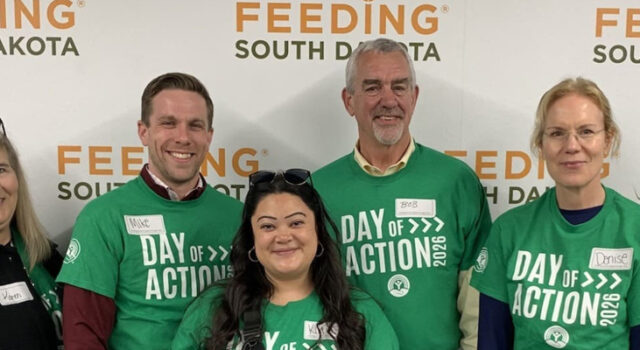 A photo of Sioux Falls Development Foundation staff wearing Day of Action shirts in front of a Feeding South Dakota backdrop