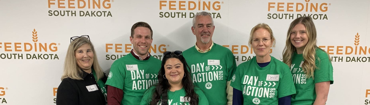 A photo of Sioux Falls Development Foundation staff wearing Day of Action shirts in front of a Feeding South Dakota backdrop