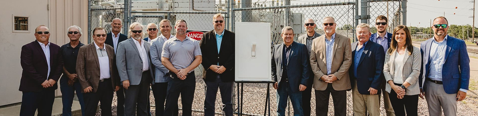A photo of people standing next to a large light switch with a power substation in the background