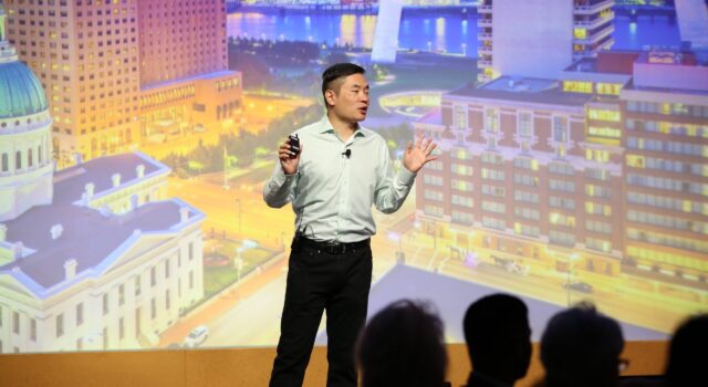Jia Jiang speaking with a cityscape backdrop behind him